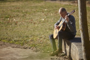 Image of Martí Batalla sitting on a stone bench next to a meadow playing the guitar