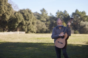 Image of Martí Batalla standing in a meadow with his guitar and harmonica