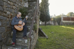 Imatge de Martí Batalla sentat a una escala d'un casa rústica tocant la guitarra i l'armònica
